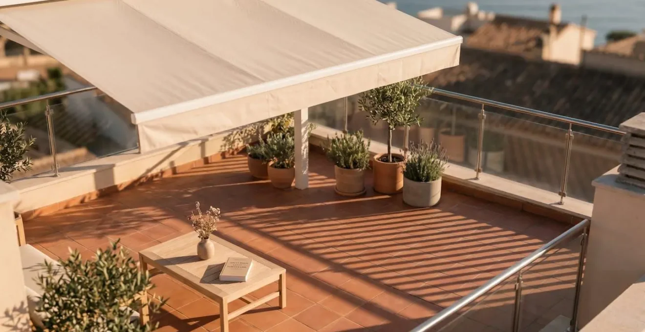 Vue aérienne d'une terrasse en dalles terracotta avec store banne déployé créant une zone d'ombre géométrique, table basse et plantes sous l'ombrage, lumière dorée du soir