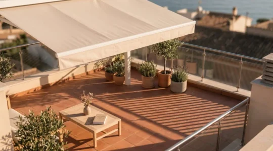 Vue aérienne d'une terrasse en dalles terracotta avec store banne déployé créant une zone d'ombre géométrique, table basse et plantes sous l'ombrage, lumière dorée du soir
